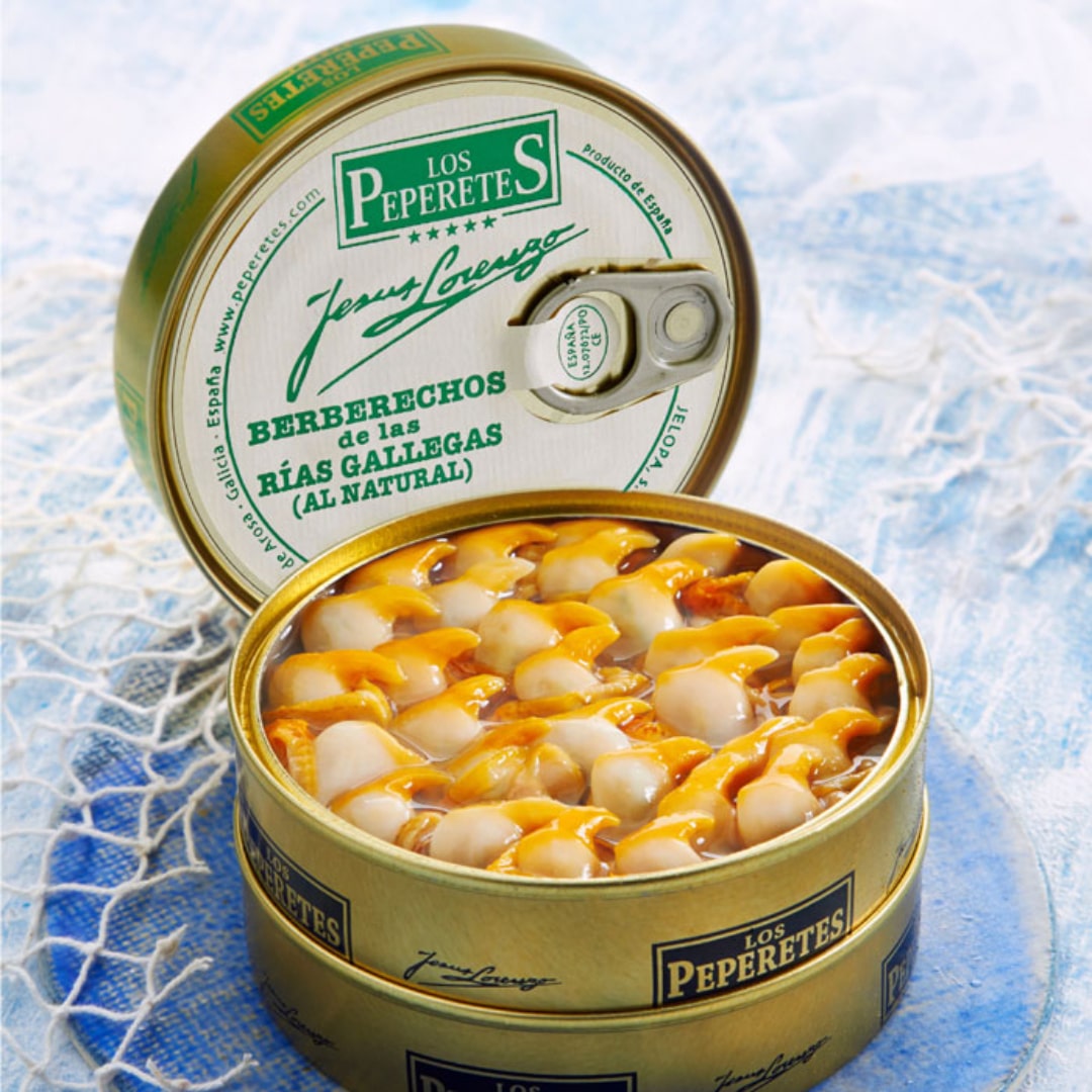 An open can of LOS PEPERETES Galician Cockles 60-70 pcs unveils tender seafood, resting on a light blue textured surface with a white mesh accentuating the authenticity of Spanish delicacies.