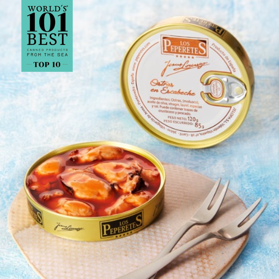 Two tins of LOS PEPERETES Oysters in Escabeche, a top Spanish delicacy by Los Peperetes, are on a blue surface. An open tin reveals Galician oysters in marinade. A fork and pronged utensil lie nearby beside the Worlds 101 Best Canned Products from the Sea Top 10 label.